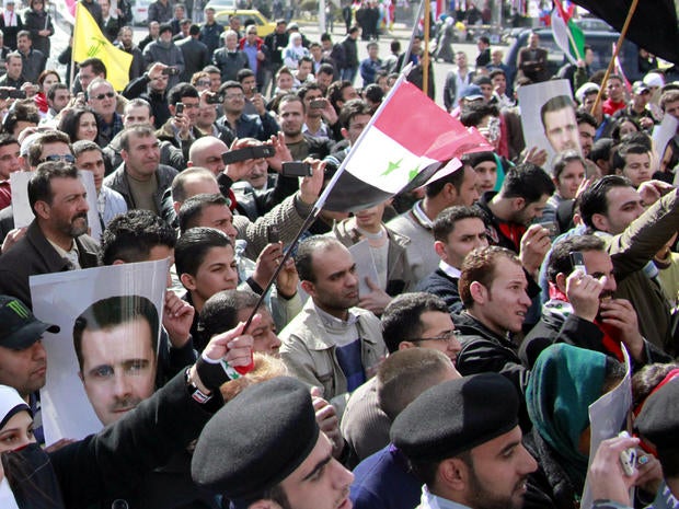 Syrian supporters of President Bashar al-Assad hold his portrait as they wave their national flag during a pro-regime demonstration at Sabe Bahrat Square in Damascus, Syria, Feb. 12, 2012.