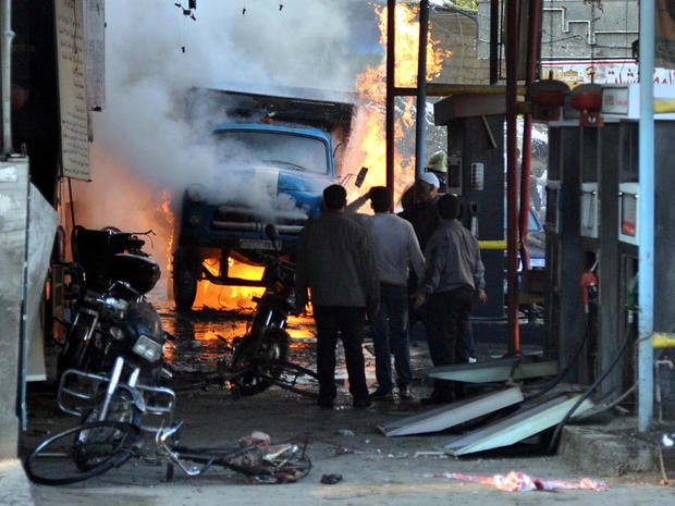 Syrians stand near a burning truck that was destroyed by two car bombs in the Jaramana suburb of Damascus, Syria, Nov. 28, 2012, in this photo released by the Syrian official news agency SANA.