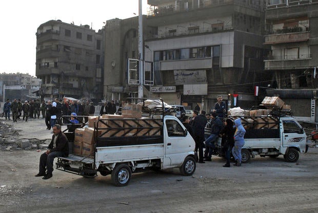 In this photo released by the Syrian official news agency SANA, trucks carry U.N. supplies at the besieged refugee camp of Yarmouk on the southern edge of the Syrian capital of Damascus