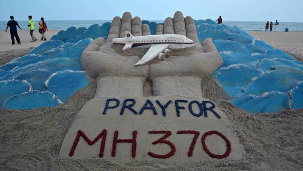 Beachgoers walk past a sand sculpture made by Indian sand artist Sudersan Pattnaik with a message of prayers for the missing Malaysian Airlines Flight MH370 at Puri beach in India March 12, 2014.