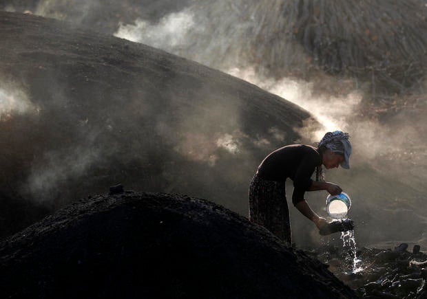 A woman sprays water on burning woods during a charcoal making process near Kizilcahamam