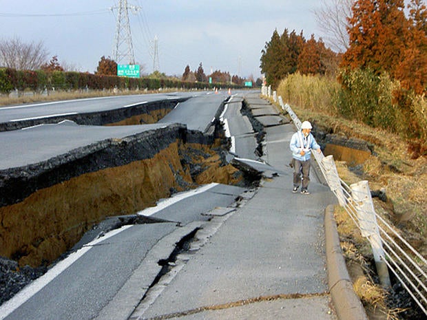 After earthquake in japan, worker examines road.