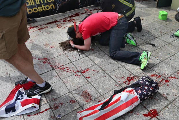 A man comforts a victim on the sidewalk at the scene of the first explosion near the finish line of the 117th Boston Marathon.