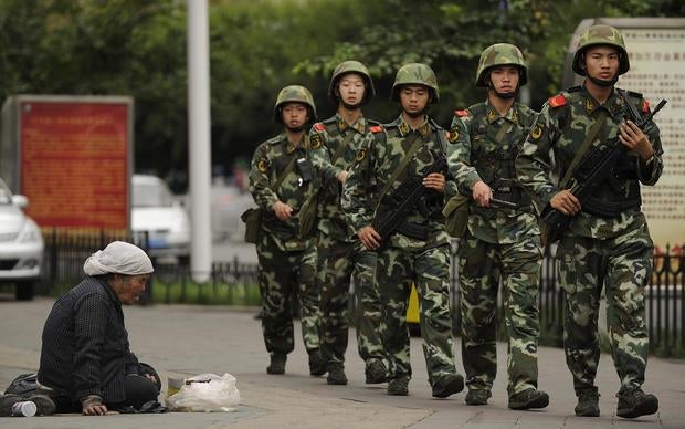 A Muslim Uighur woman begs as armed Chinese paramilitary police march past on a street in Urumqi, the capital of the Xinjiang region