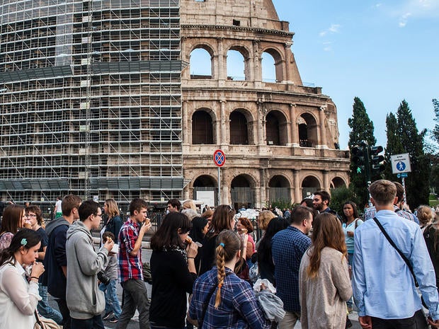 Tourists and locals walk in front of the Colosseum, partially covered in scaffolding weeks before restoration work began, Oct. 9, 2013 in Rome