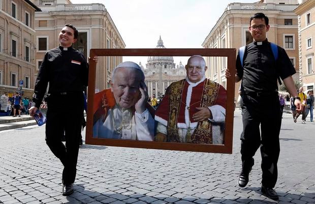 Two priest walk carrying pictures of Pope John Paul II (L) and Pope John XXIII in front of St. Peter's square