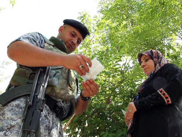 A member of the Iraqi security forces checks identities as voters arrive to cast their ballot in Iraq's first parliamentary election since U.S. troops withdrew at a polling station in Baghdad's Sadr City district