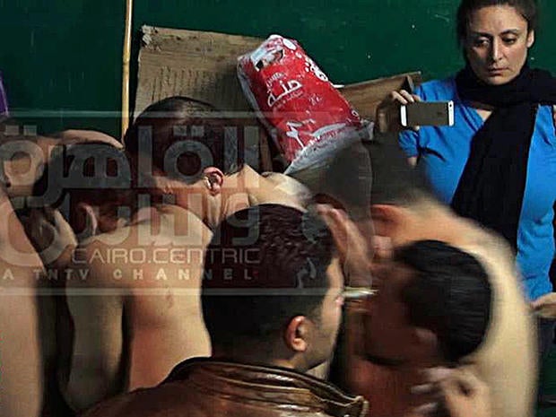 An image from Egyptian satellite channel Al-Qahira wa al-Nas shows journalist Mona Iraqi, (rear, right) photographing men arrested during a police raid on a public bathhouse in Cairo