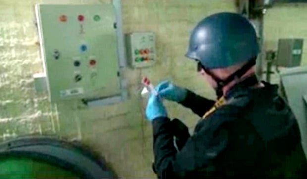 This file image made from video broadcast on Syrian State Television on Oct. 8, 2013, purports to show a chemical weapons expert taking samples at a chemical weapons plant at an unknown location in Syria.