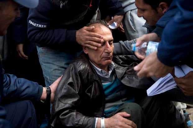 Greek police and migrants help a man who fainted after being turned back by Macedonian border authorities at the Idomeni crossing because of irregularities in his identity papers, near the northern Greek village of Idomeni