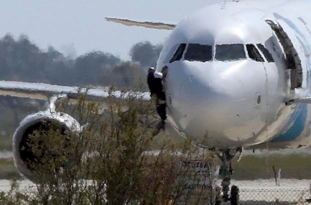A man climbs out of the cockpit window of the hijacked Egyptair Airbus A320 at Larnaca Airport in Larnaca