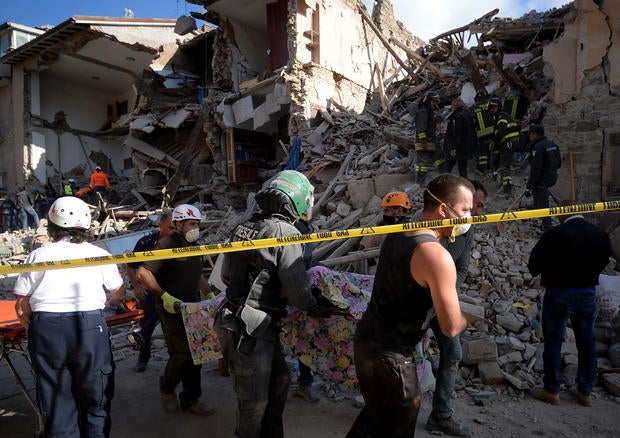 Rescuers carry the body of a victim next to the rubble of buildings in Amatrice