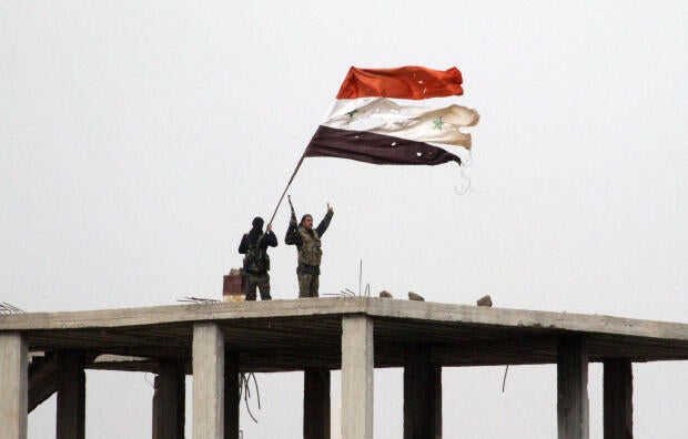 Syrian government forces wave the Syrian flag while standing on top of a building in Deir al-Adas, Syria, on Feb. 11, 2015, after President Bashar Assad&rsquo;s army, backed by Hezbollah and Iranian officers, pushed rebels out of the area. 