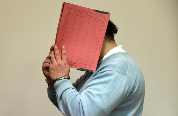 Former nurse Niels H. masks his face with a folder on his arrival in the courtroom in Oldenburg