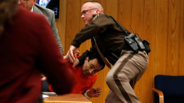 An Eaton County sheriff's deputy protects Larry Nassar, wearing orange, a former USA Gymnastics team doctor who pleaded guilty in November 2017 to sexual assault charges, as he is attacked by Randall Margraves, not pictured, during victim statements in his final sentencing hearing in Eaton County Circuit Court in Charlotte, Michigan, Feb. 2, 2018. 