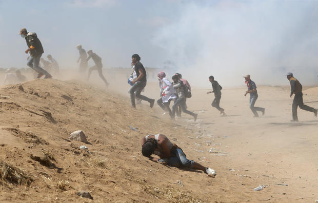 Palestinian demonstrator reacts as others run from tear gas fired by Israeli forces during a protest marking the 70th anniversary of Nakba, at the Israel-Gaza border in the southern Gaza Strip 