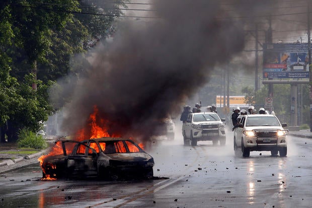 Riot police officers travel past a burning car during clashes with the anti-government protesters in Managua, Nicaragua