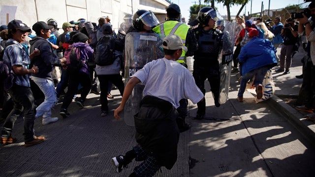 Migrants break past a line of police as they run toward the Chaparral border crossing in Tijuana, Mexico, Nov. 25, 2018, near the San Ysidro entry point into the U.S.