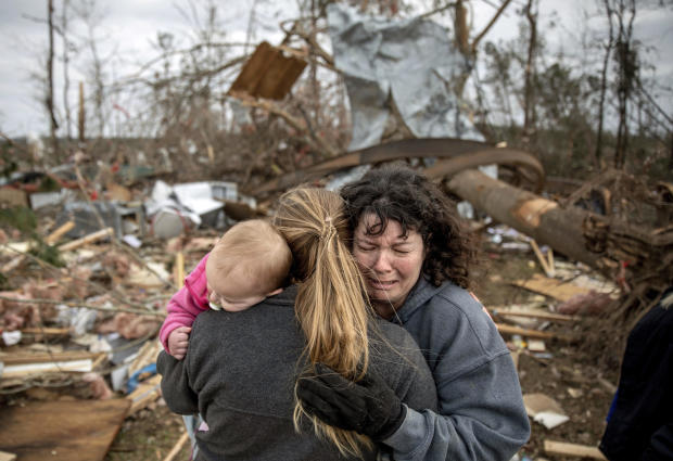 Carol Dean, right, cries while embraced by Megan Anderson and her 18-month-old daughter Madilyn as Dean sifts through the debris of the home she shared with her husband, David Wayne Dean, who died when a tornado destroyed the house in Beauregard, Alabama, 
