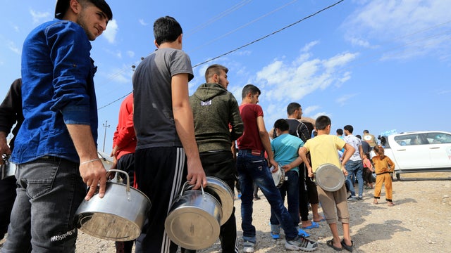 Syrian displaced families, who fled violence after the Turkish offensive in Syria, stand in queue to get their food from Barzani charity at a refugee camp in Bardarash on the outskirts of Dohuk 