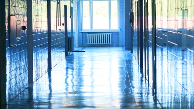 Blurry photo of hospital walk way with bright blue lighting. White floor with cool tone color with light tunnel in the middle of picture. 