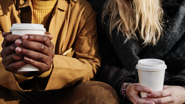 Friends holding a paper cup of coffee while sitting together. focus on the hands. 