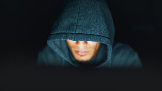 Hoodie-wearing young man looks sinister, working on computer at night 